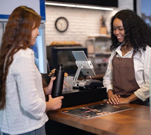 A smiling shopper scanning a QR code with their phone at a checkout counter.